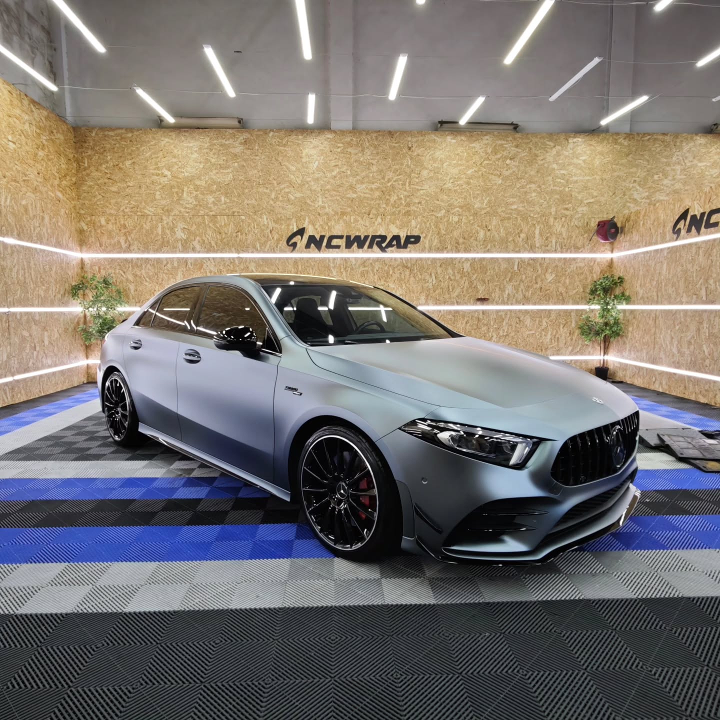 Luxury sports sedan cloaked in a metallic grey car wrap reflecting an icy blue car wrap shadow variance under workshop lighting.