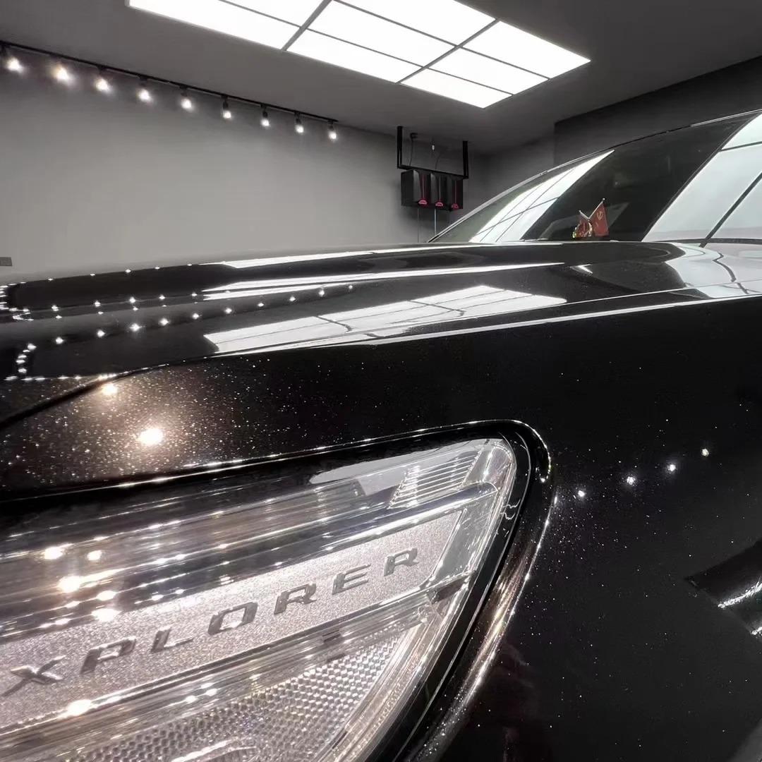 Luxury sports sedan featuring a stealthy, deep Santorini Black Car Wrap under moody showroom spotlights.