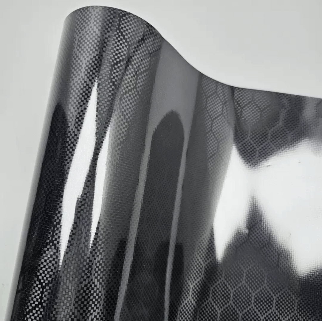 Close-up texture of gloss honeycomb carbon fiber black car vinyl wrap roll with premium PET backing.