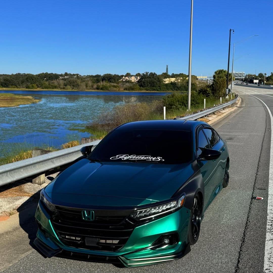 Side view of a prestige luxury sports car wrapped in premium gloss metallic emerald green vinyl, revealing a rich jewel-like reflective luster under sunny day conditions.