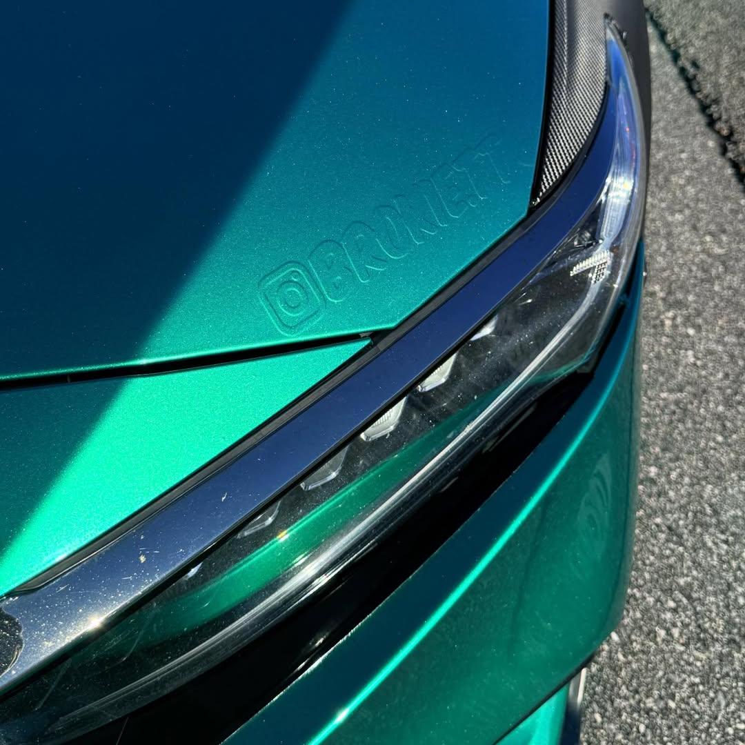 Micro detail shot of a high-gloss metallic green vinyl wrap film molded on a vehicle fender, presenting a flawless liquid-like deep paint imitation.