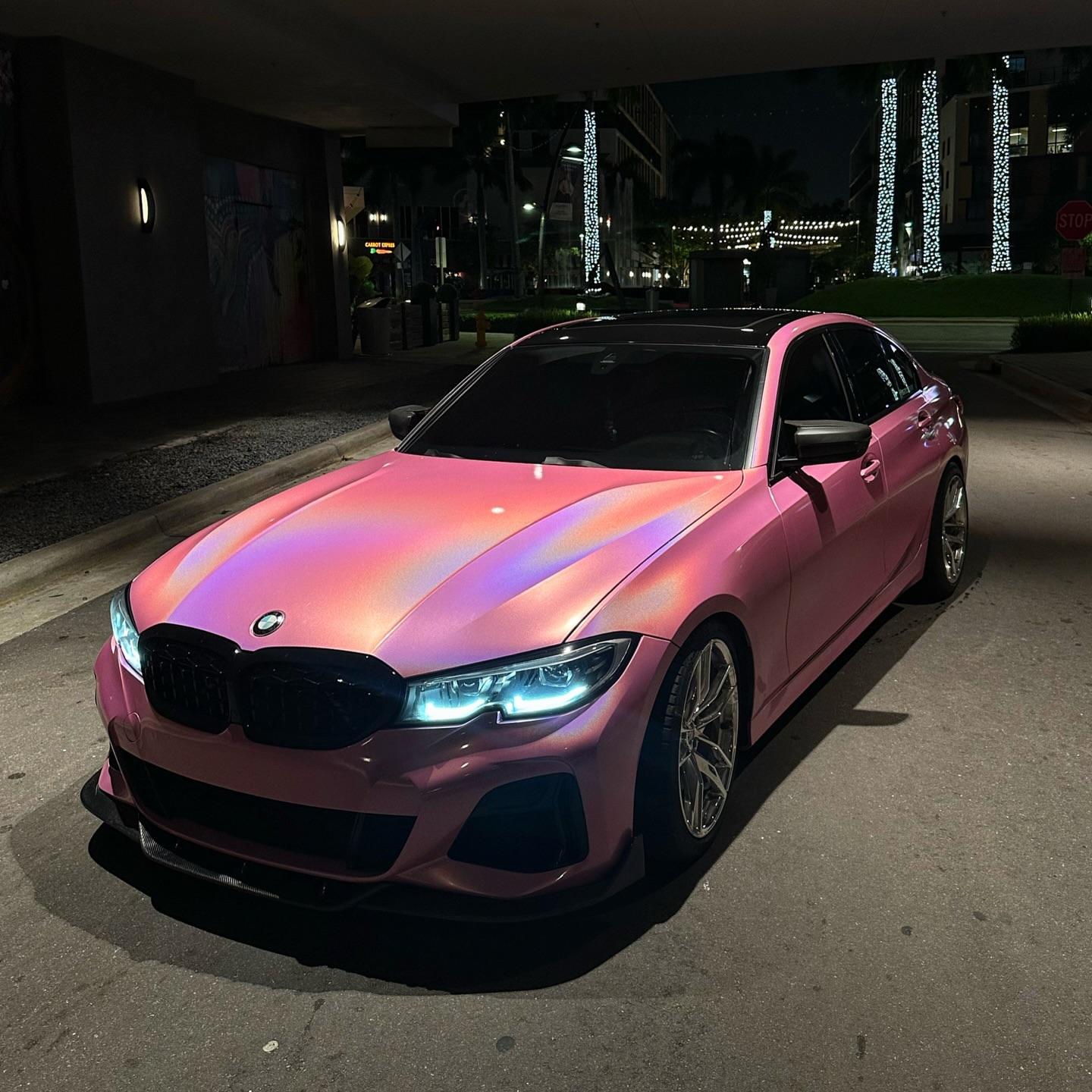 A trendy luxury car wrapped in Gloss Metallic Rainbow Laser Pink Car Vinyl Wrap PET, capturing vibrant holographic flares.