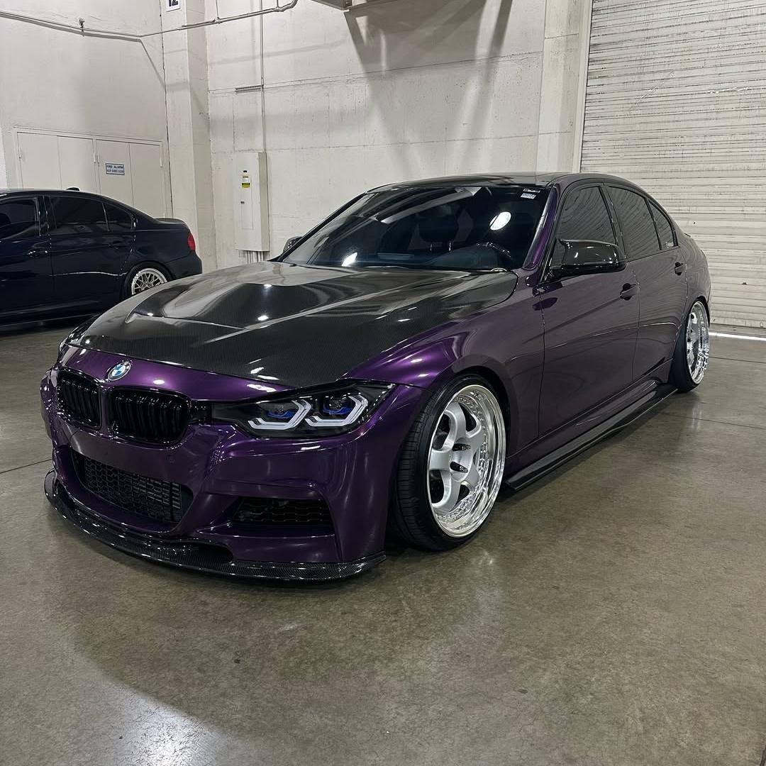 A futuristic EV coupe wrapped in Gloss Metallic Twilight Purple car vinyl, parked on wet asphalt under nighttime neon city streetlights.