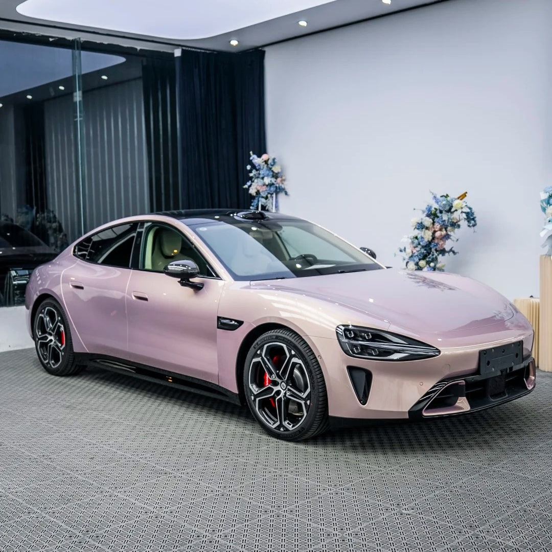 A luxury sports car transformed with a full gloss metallic gilded rose pink wrap exhibiting radiant reflections under open sunlight.