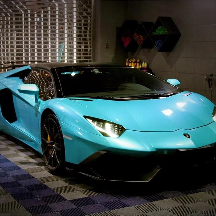 ALUKOCARWRAP Ocean Blue Car Wrap wrapping a luxury sedan as it distorts bright city streetlights and vibrant night-time neon signs.