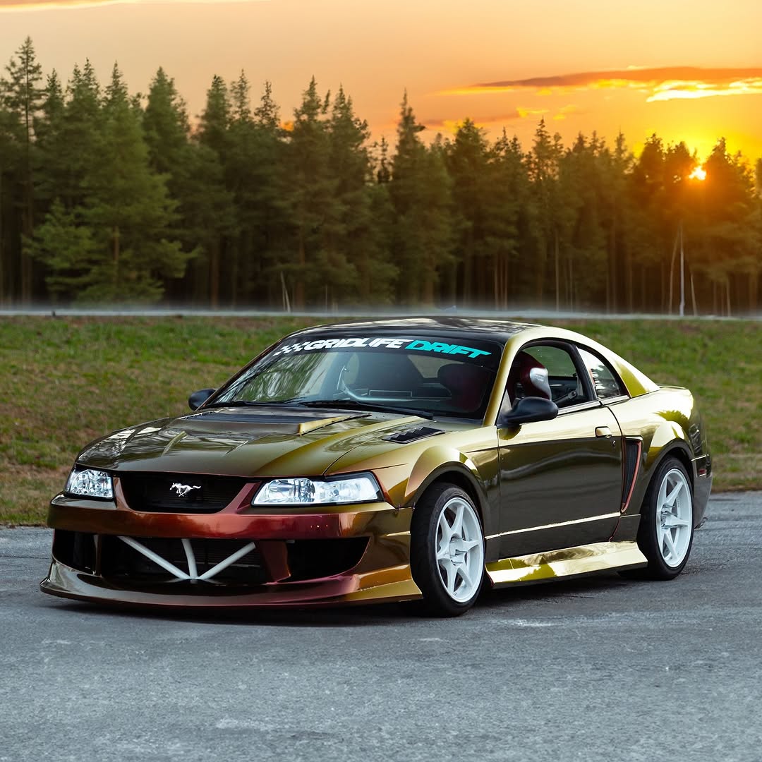 A sportscar completely covered in ALUKOCARWRAP Sunrise Morning Car Wrap, displaying a dramatic liquid gold and deep red metallic shift across the car doors and quarter panels.